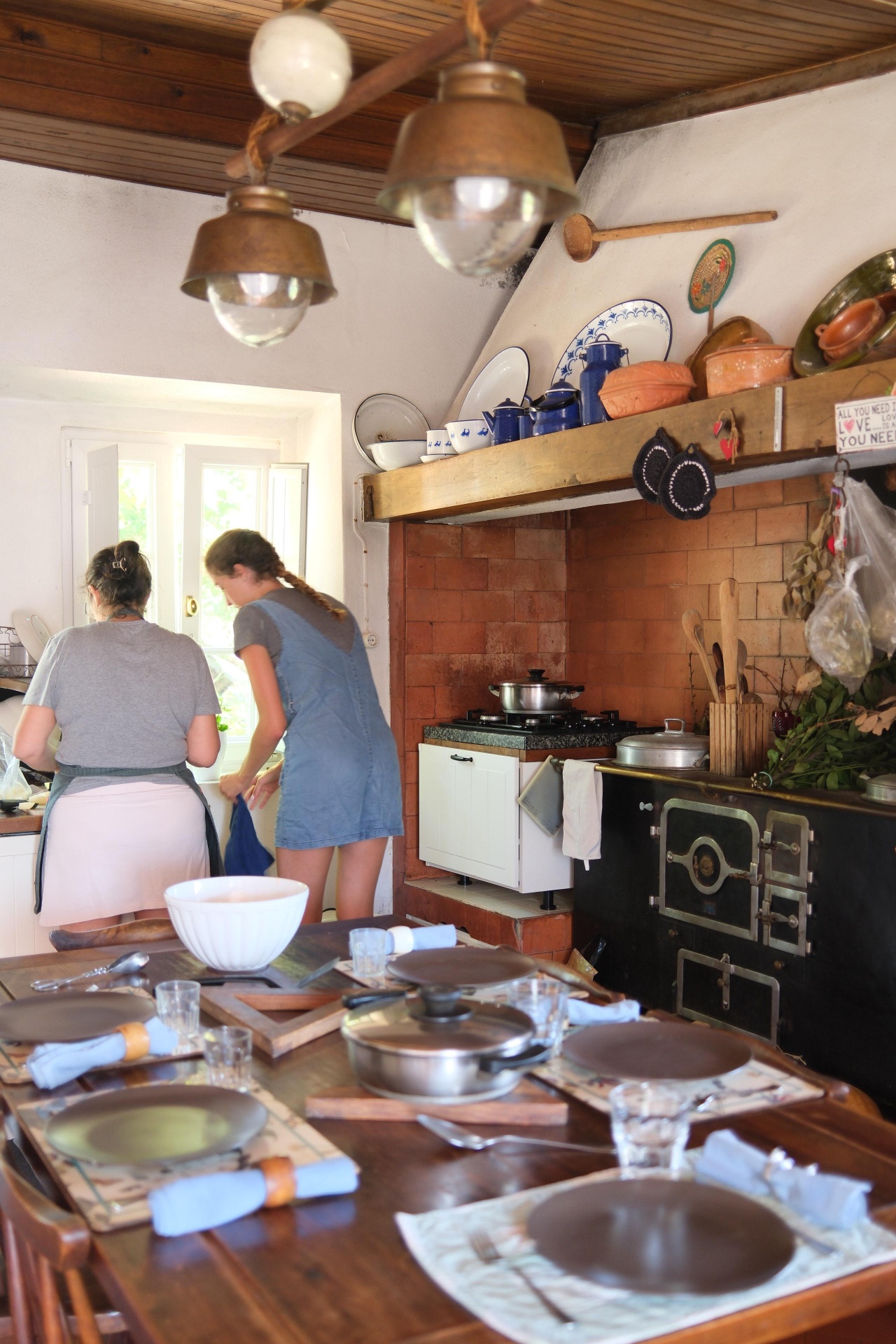 Two women cooking in a rustic farmhouse kitchen with a set table