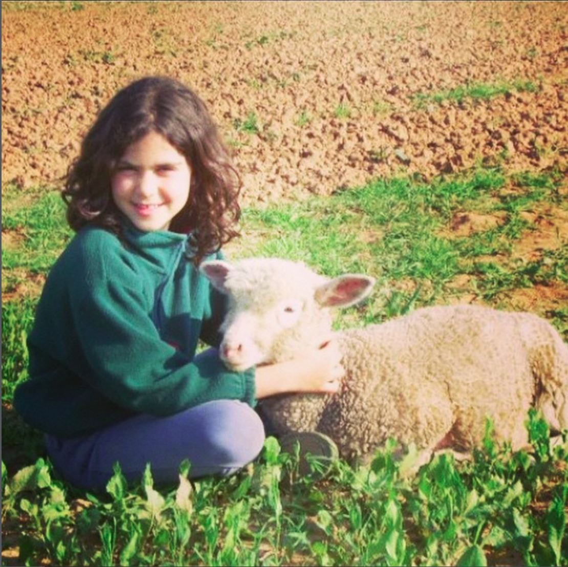 Maria as a child sitting in a field beside a lamb